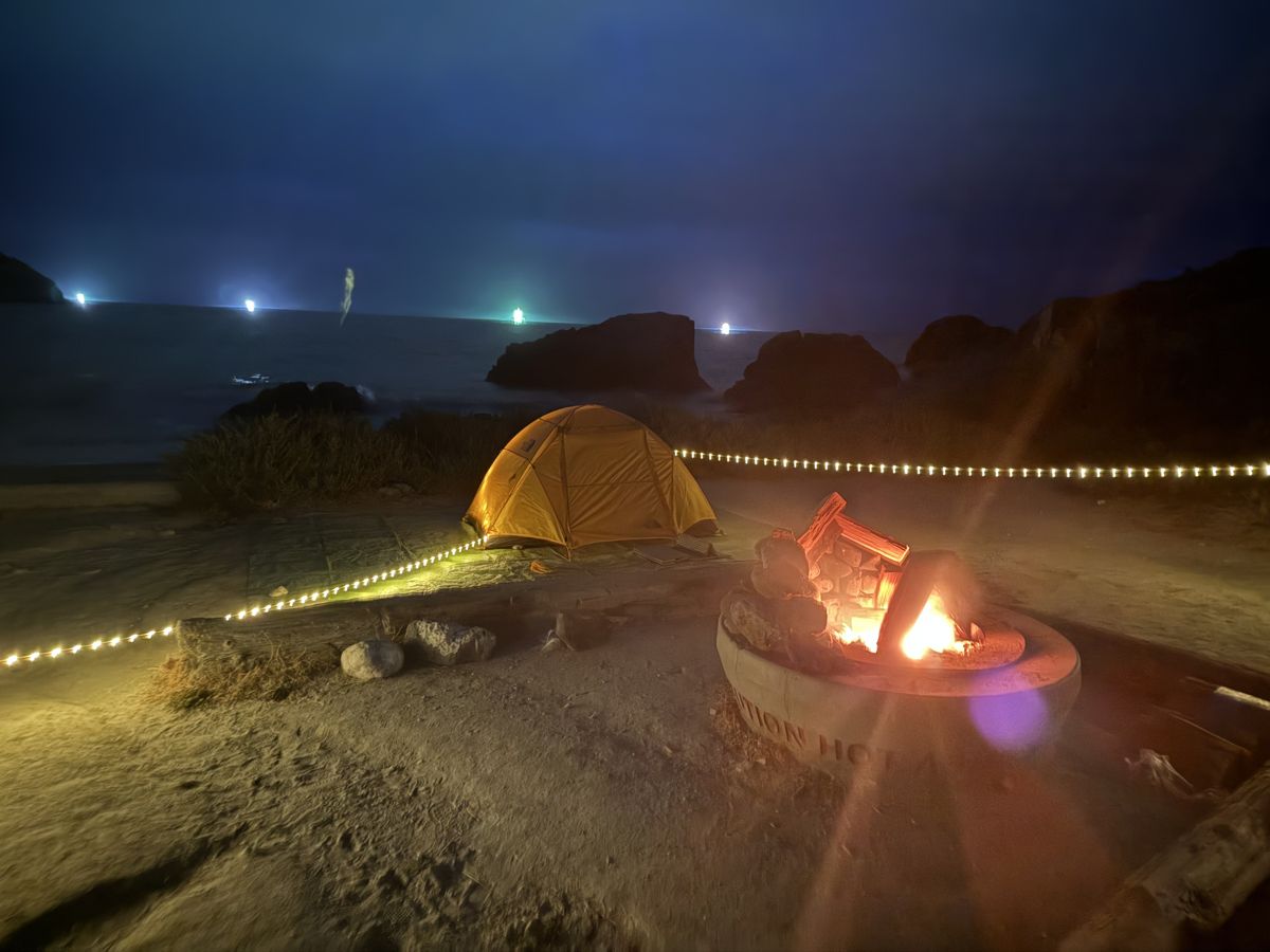 A yellow tent at night by the ocean with a fire ring at Shark Harbor on the Trans-Catalina Trail