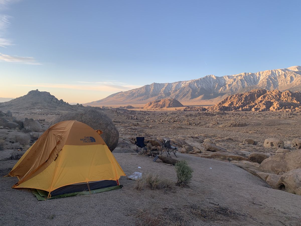 A tent among desert boulders at sunrise with the snowy Sierra Nevada behind, in the Alabama Hills
